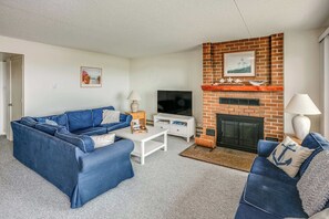 Ein Wohnzimmer mit Kamin aus Backsteinen, einem blauen Sofa, einem weißen Couchtisch und einem Fernseher.