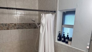Ein Badezimmer mit Dusche, Toilette, Waschbecken und einem Fenster mit Pflegeprodukten.
