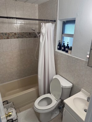 Ein Badezimmer mit Dusche, Toilette, Waschbecken und einem Fenster mit Pflegeprodukten.