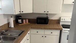 Eine Küche mit weißen Schränken, einer Mikrowelle, einer Kaffeemaschine, einem Spülbecken und einem Herd.