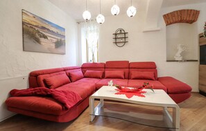Ein Wohnzimmer mit einem roten Ecksofa, einem Glastisch, Pendelleuchten, einem Gemälde und einem Kamin aus Ziegelsteinen.