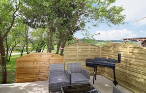 Ein Holz-Sitzbereich im Freien mit Grill und Korbstühlen.