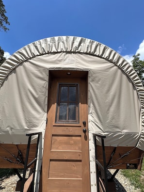 A wooden door with a window, a tent-like structure, and the name 'CONESTOGA' on the door. - Conestoga Covered Wagon on Working Farm - Willowmere (Fredericktown)