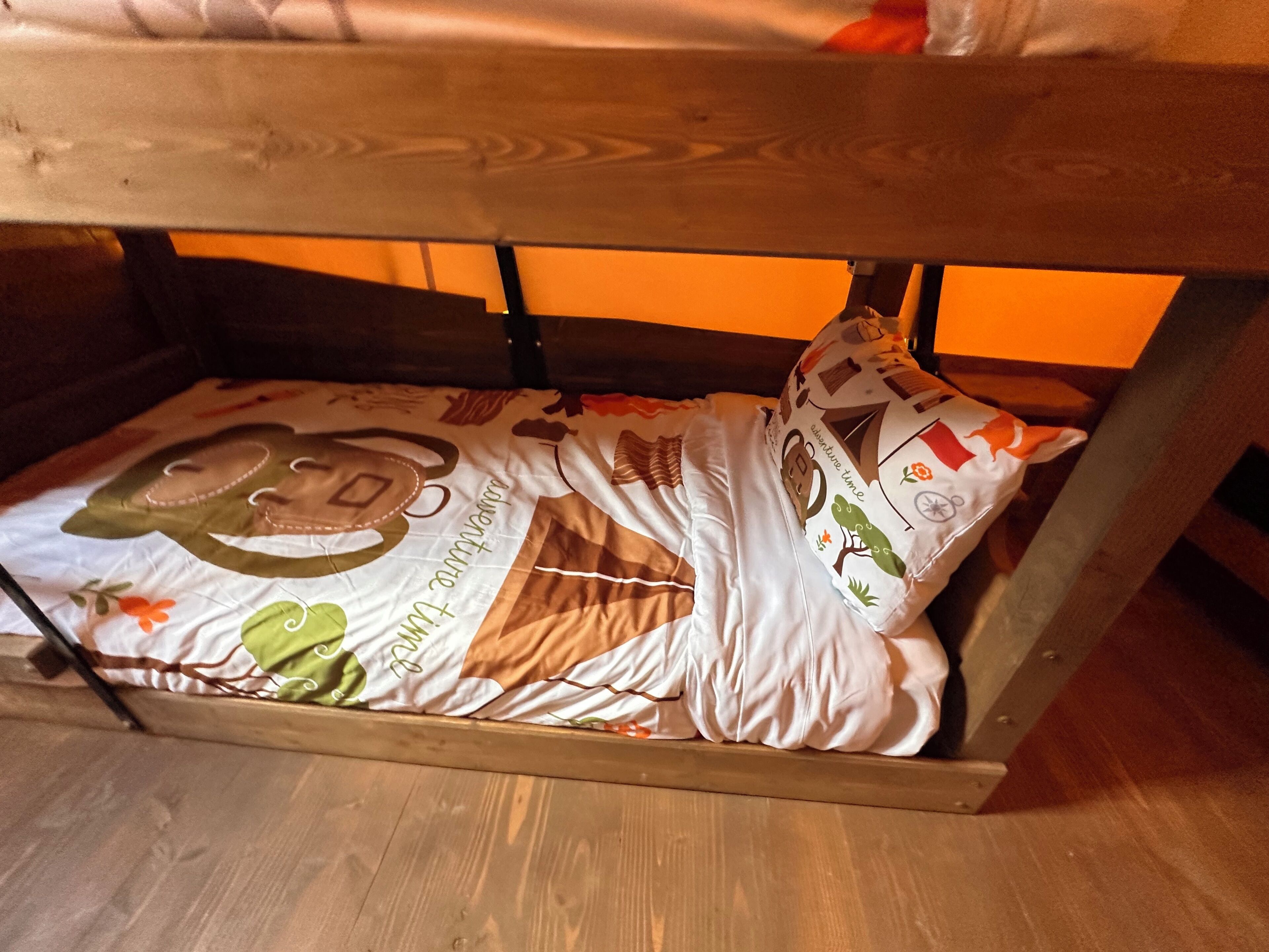 A bunk bed with a patterned bedspread and pillows, wooden headboard, and a wooden floor.