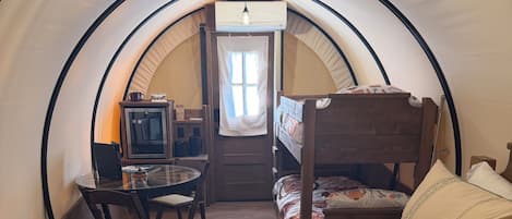 Une pièce confortable aménagée sous une tente, avec un lit, une petite table et une chaise.