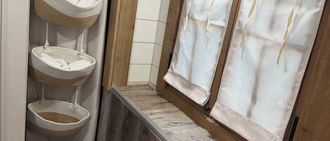 A bathroom with a wooden vanity, a hanging basket, and a window with curtains.