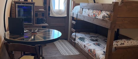 A cozy room with a bunk bed, a small table with a chair, a desk with a computer, and a window with curtains.
