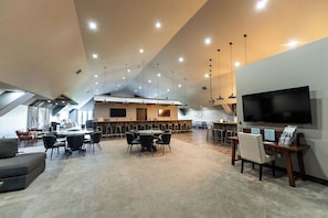Una amplia sala de conferencias con una gran mesa, varias sillas, una zona de bar y un televisor en la pared.