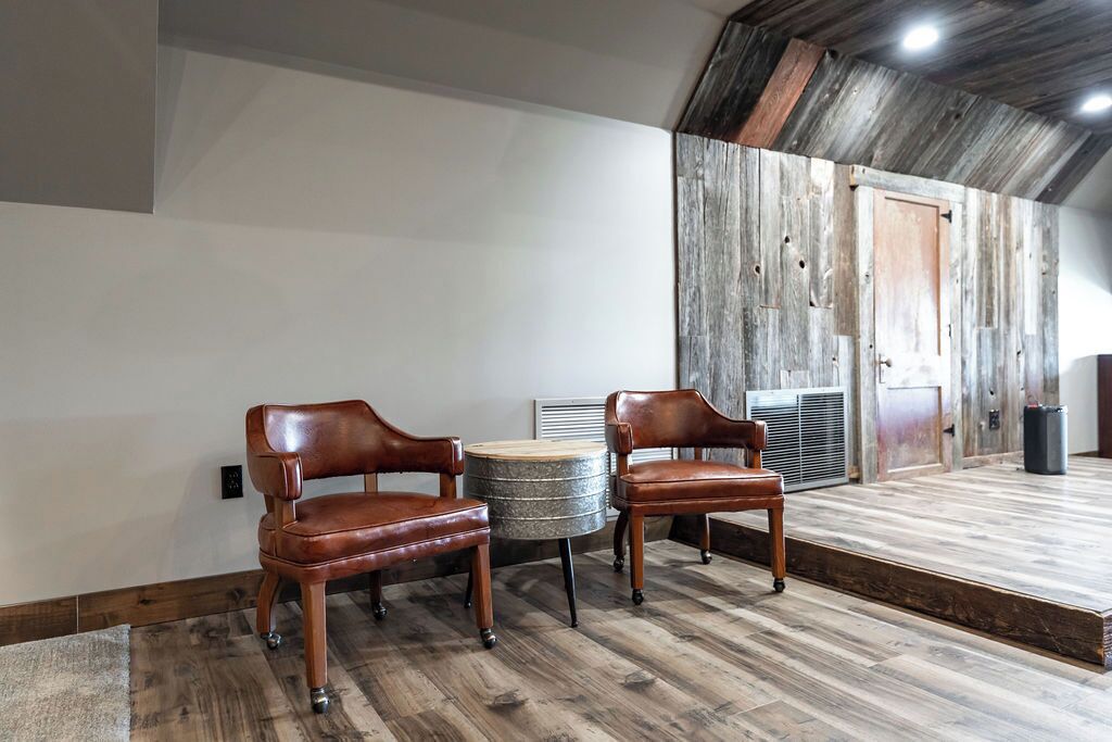 Una habitación con dos sillones de cuero, una mesa redonda de metal y una pared de madera con una puerta.