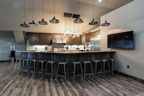 Una cocina moderna con una isla central, taburetes de bar, lámparas colgantes y un televisor de pantalla plana grande montado en la pared.
