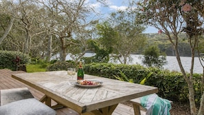 Eine Holzterrasse mit einem Tisch für zwei Personen, einer Champagnerflasche und einer Obstplatte.