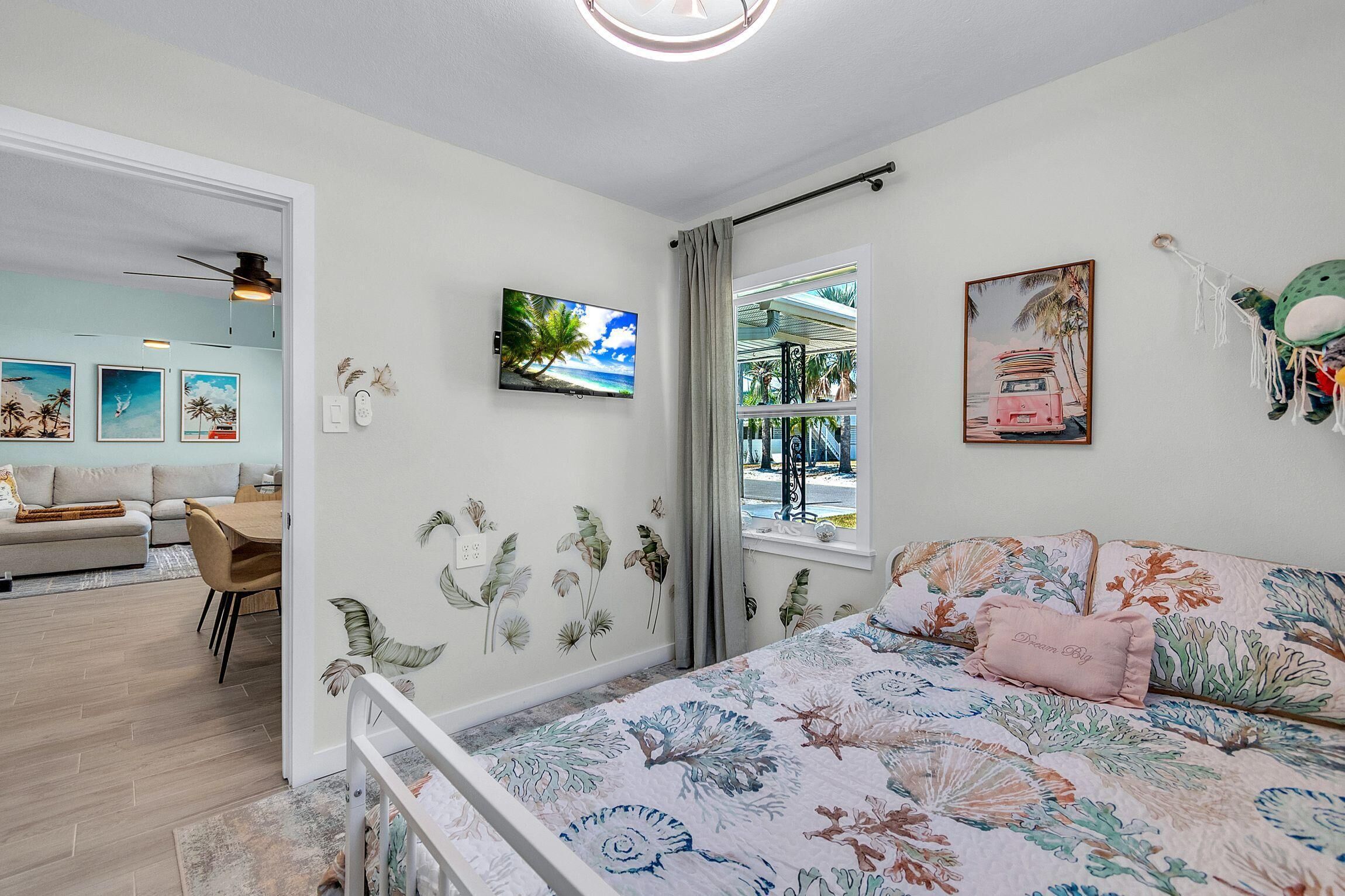 Une chambre à coucher avec un lit, une fenêtre donnant sur un beau paysage, un ventilateur de plafond et des œuvres d’art murales.