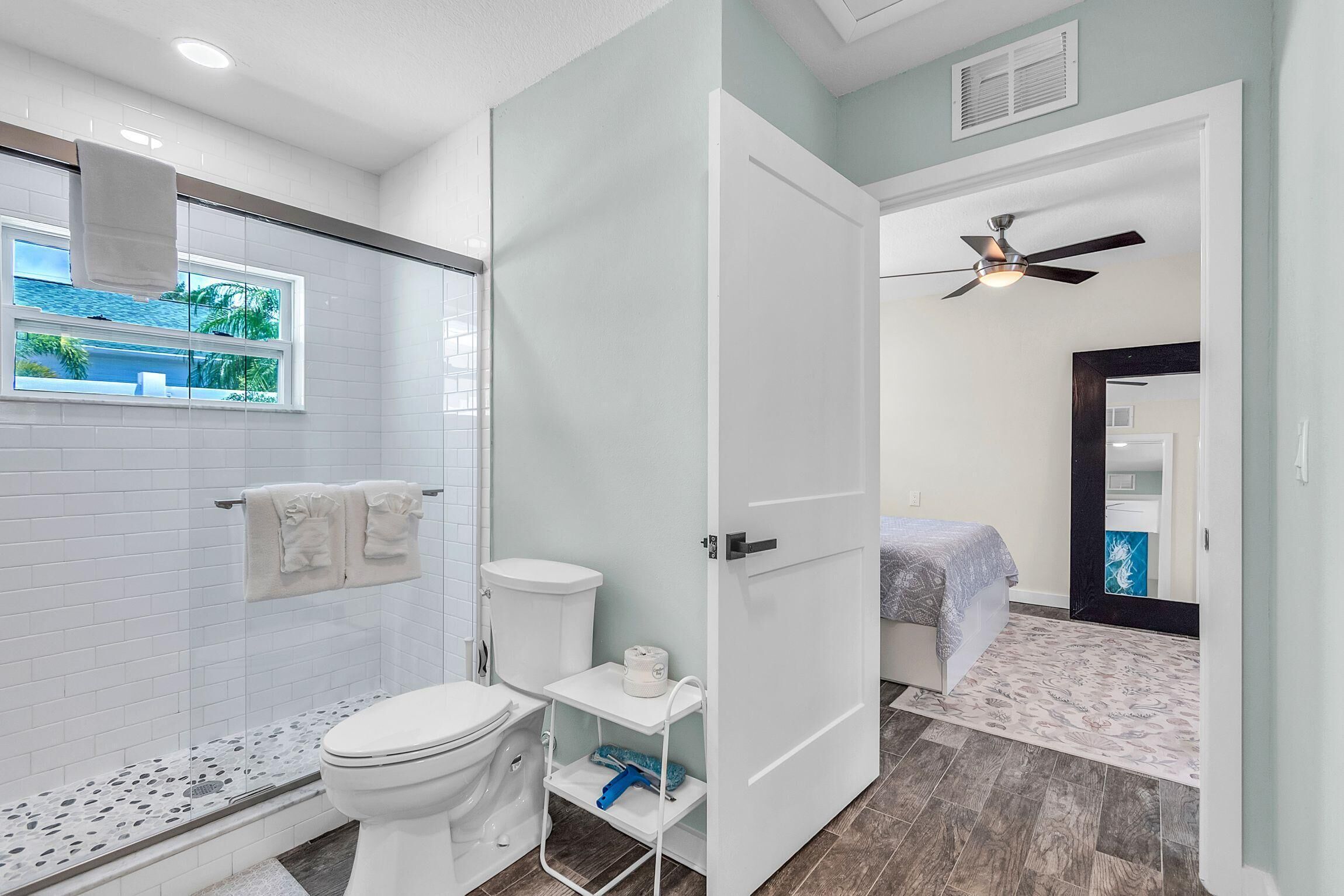 A bathroom with a toilet, a shower, and a window with a towel hanging.