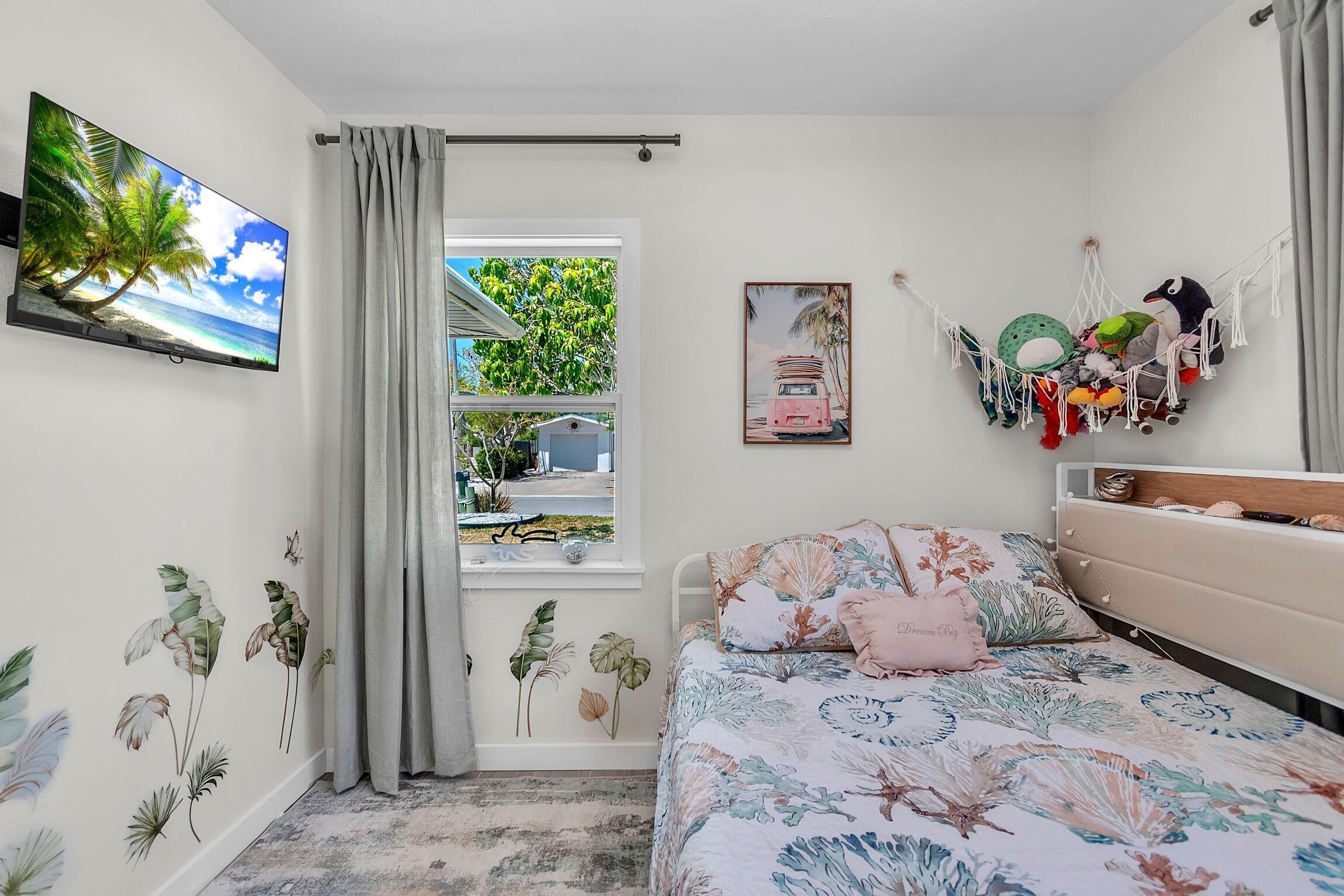 Een slaapkamer met een bed, een televisie, een raam met gordijnen en wanddecoratie.