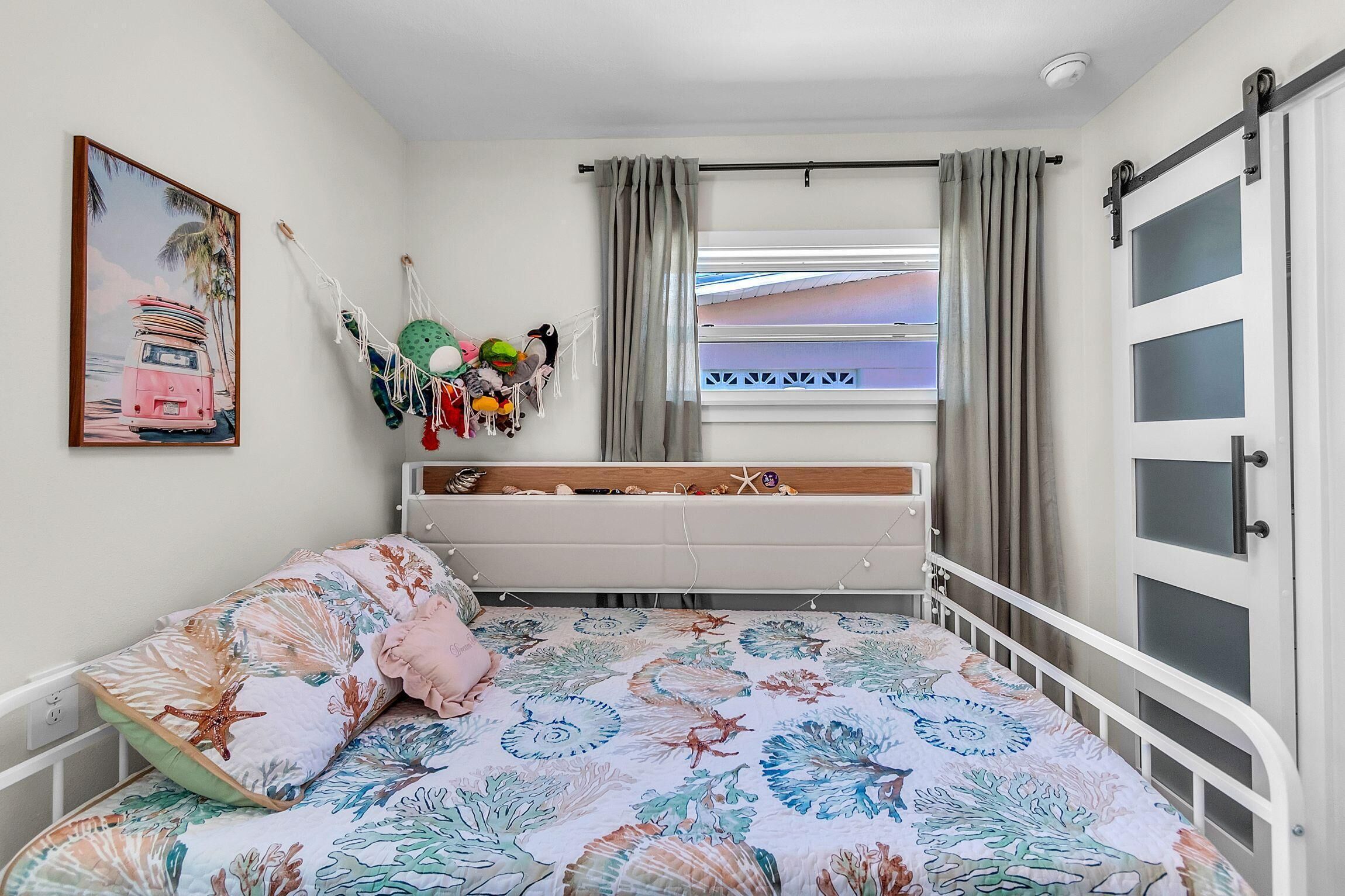 Un dormitorio con cama, ventana con cortinas, puerta y un adorno en la pared.