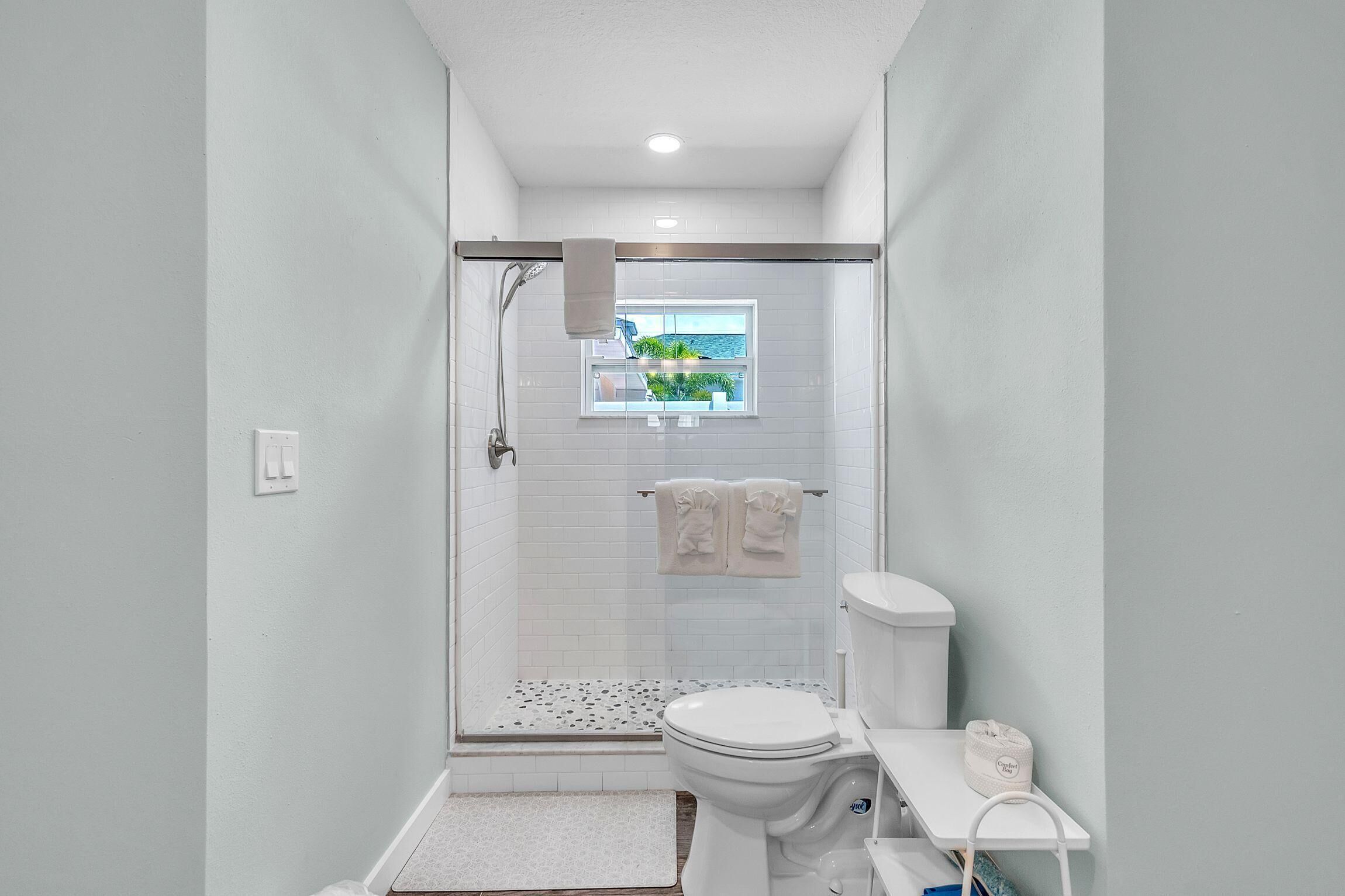Een badkamer met douche, toilet en een klein raam.