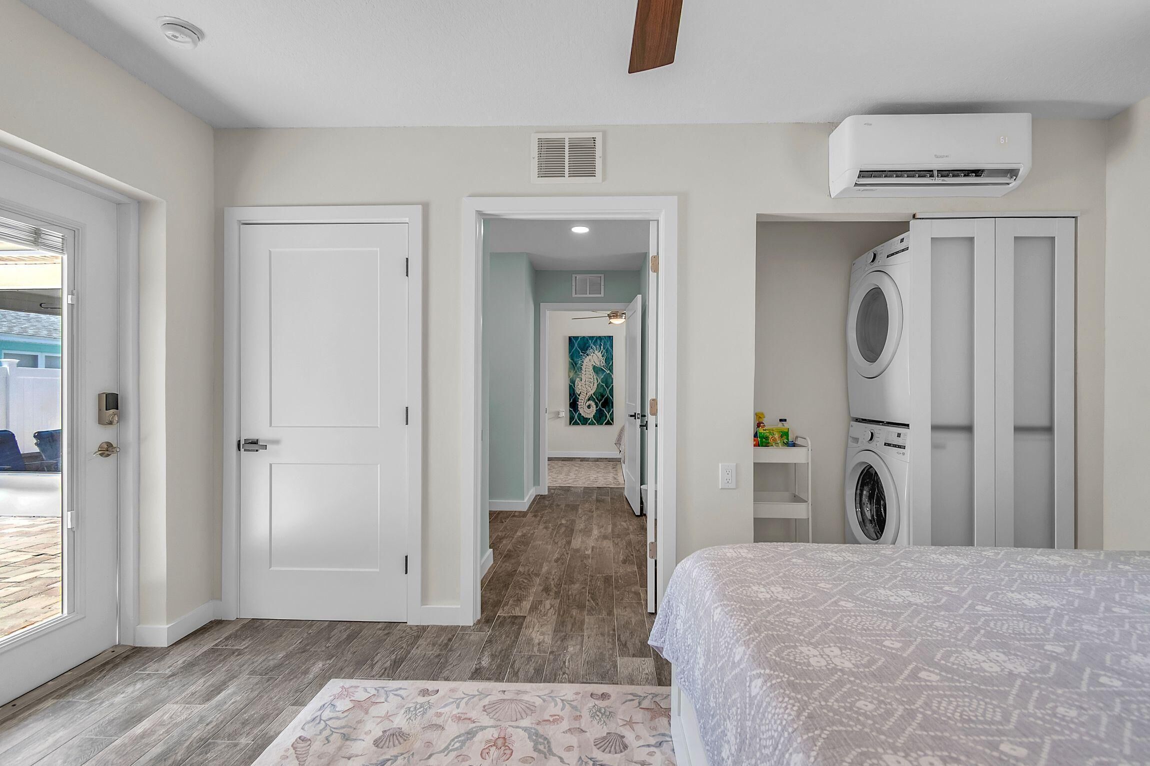A bedroom with a bed, an air conditioning unit, a washing machine, and a hallway leading to another room.
