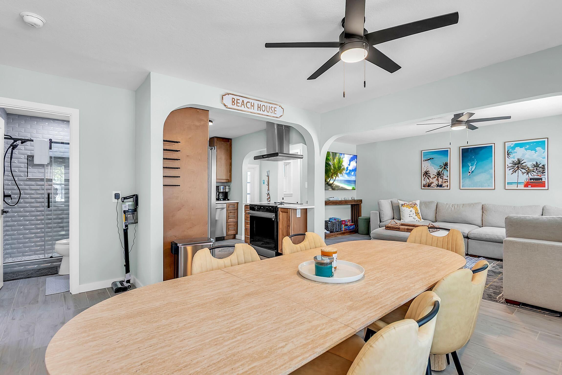 A modern kitchen with a central island, a dining area with a long table, and a living room with a sofa and a TV.