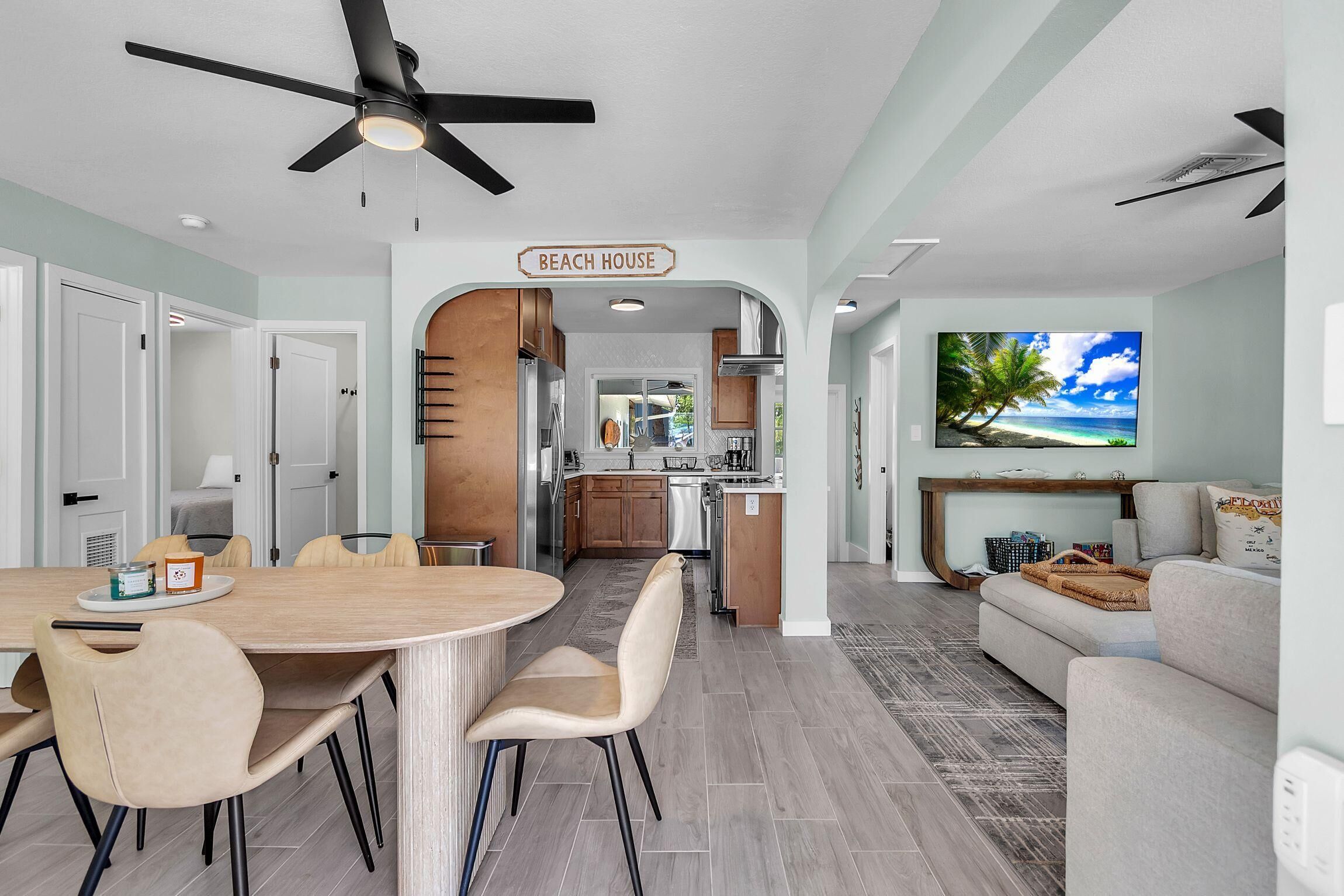 A modern kitchen with a dining area, a living room with a TV, and a ceiling fan.
