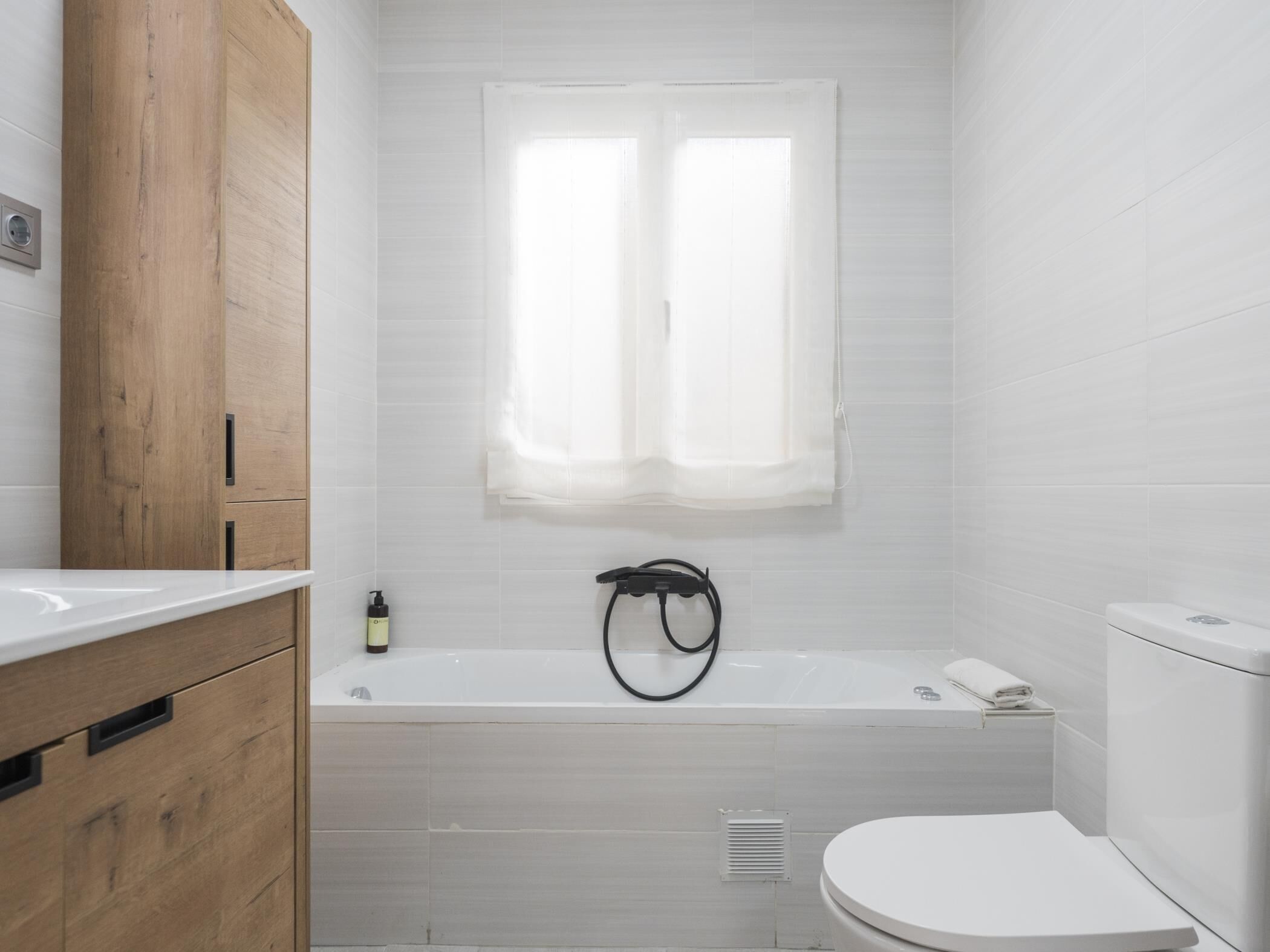Un baño moderno con un mueble de madera, una bañera, un inodoro y una ventana con cortinas.