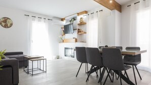 Uma sala de estar moderna com sofá, mesa de jantar com cadeiras, televisão na parede e lareira.