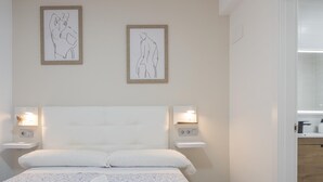Quarto de hotel com uma cama grande, duas mesas de cabeceira com abajures, uma luminária na parede e um banheiro visível através de uma porta aberta.
