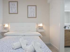 Ein Hotelzimmer mit einem großen Bett, zwei Nachttischen mit Lampen, einer Wandleuchte und einem durch eine offene Tür einsehbaren Badezimmer.