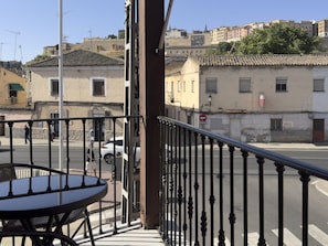 Ein Balkon mit Tisch, Blick auf eine Straße mit Gebäuden und ein Schild mit der Aufschrift 'Locker in the City'.