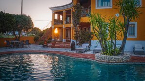 Un edificio de dos pisos con piscina, asientos al aire libre y una escalera que lleva a la entrada.