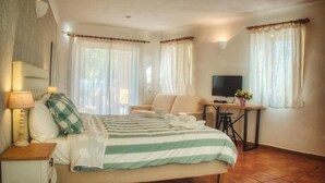 Un dormitorio con cama, escritorio, televisor y dos ventanas con cortinas.