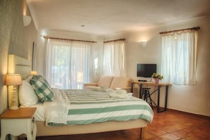 A bedroom with a bed, a desk, a TV, and two windows with curtains. - Lagos Beachfront Studio Apartment With Pool (Lagos)