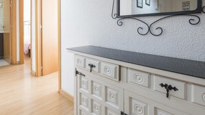 Quarto com piso de madeira, cômoda branca com várias gavetas, espelho com moldura decorativa e porta que dá para outro cômodo.