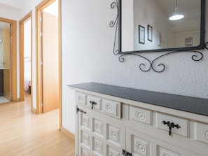 Ein Zimmer mit Holzboden, einer weißen Kommode mit mehreren Schubladen, einem Spiegel mit dekorativem Rahmen und einer Tür zu einem weiteren Raum.