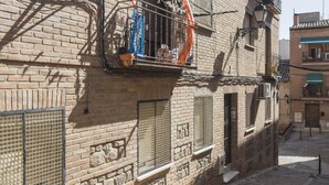 Uma rua estreita com edifícios de tijolo, uma janela visível com grade de metal e uma varanda com corrimão.