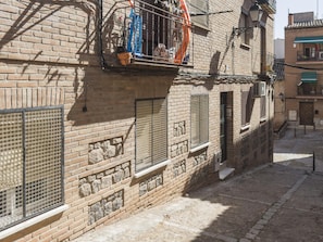 Eine schmale Gasse mit Backsteingebäuden, einem sichtbaren Fenster mit Metallgitter und einem Balkon mit Geländer.