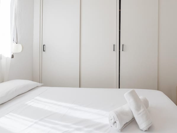 Ein Hotelzimmer mit Bett, weißen Vorhängen und einem zweitürigen Schrank.