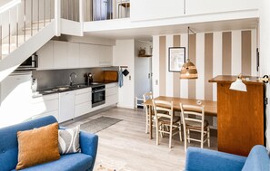 Eine moderne Küche mit weißen Schränken, ein Essbereich mit Holztisch und -stühlen sowie eine Treppe, die zu einer oberen Ebene führt.