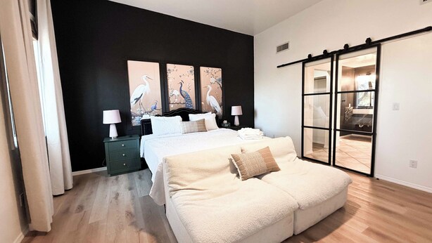 Ein Schlafzimmer mit Bett, einer Couch, einem Nachttisch, einer Lampe und einer Schiebetür zu einem Badezimmer.