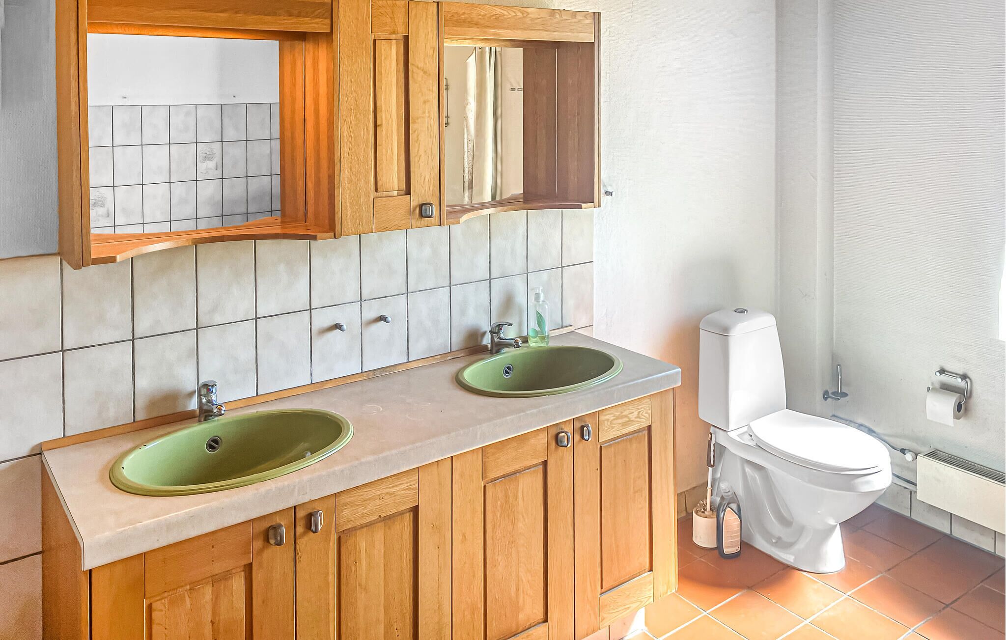 Une salle de bain avec deux lavabos verts, des meubles en bois, un miroir, des toilettes et un espace douche.