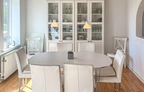 A dining area with a round table, white chairs, and a glass cabinet with kitchenware.
