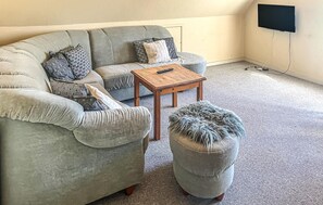 A grey sofa with patterned cushions, a small wooden table, and a grey ottoman with a fluffy cover.