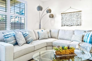 A modern living room with a sectional sofa, a glass coffee table, and decorative wall art.