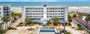 A beachfront hotel with multiple floors, a swimming pool, and palm trees. - Boardwalk 401 (Cocoa Beach)