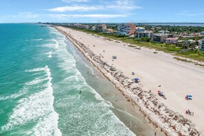 A beach with a long stretch of sand, a pier, and buildings in the background. - 7015 Orange Ave (Cape Canaveral)