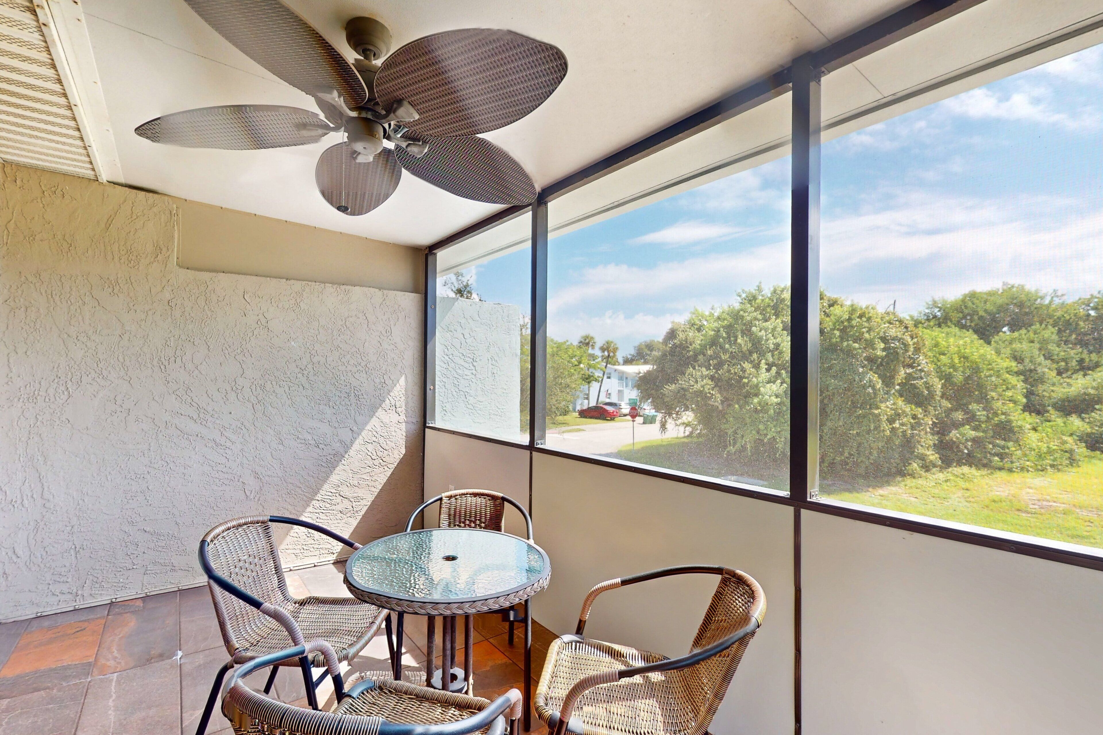 A balcony with wicker chairs, a glass table, and a ceiling fan.