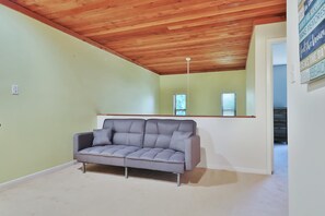 Ein Zimmer mit grauem Sofa, Holzboden, hellgrünen Wänden und einem Fenster mit Jalousien.
