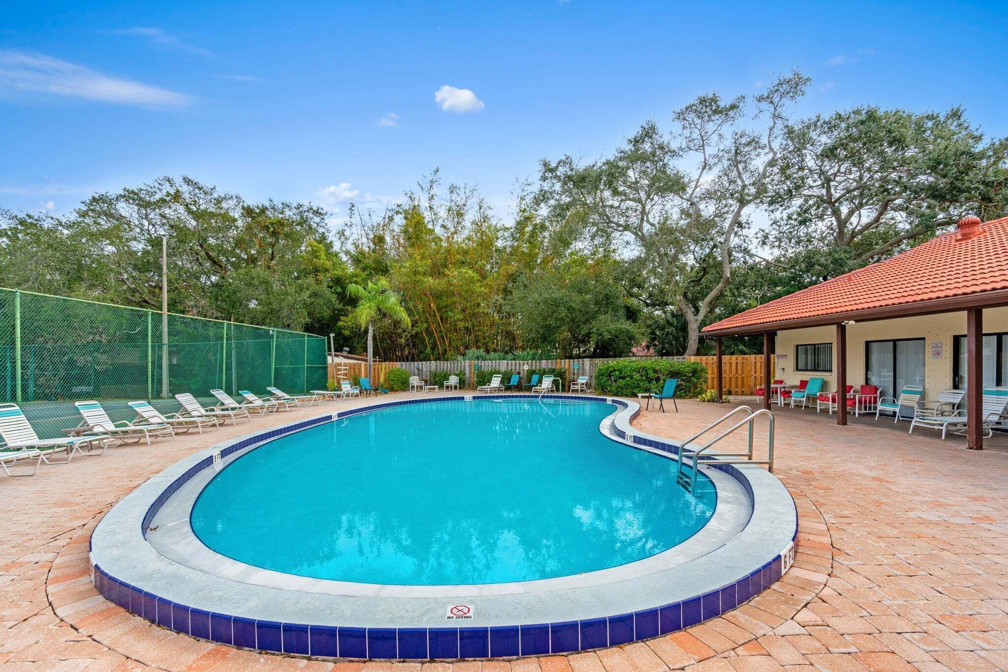 A swimming pool with a tiled edge, surrounded by lounge chairs and a fence.