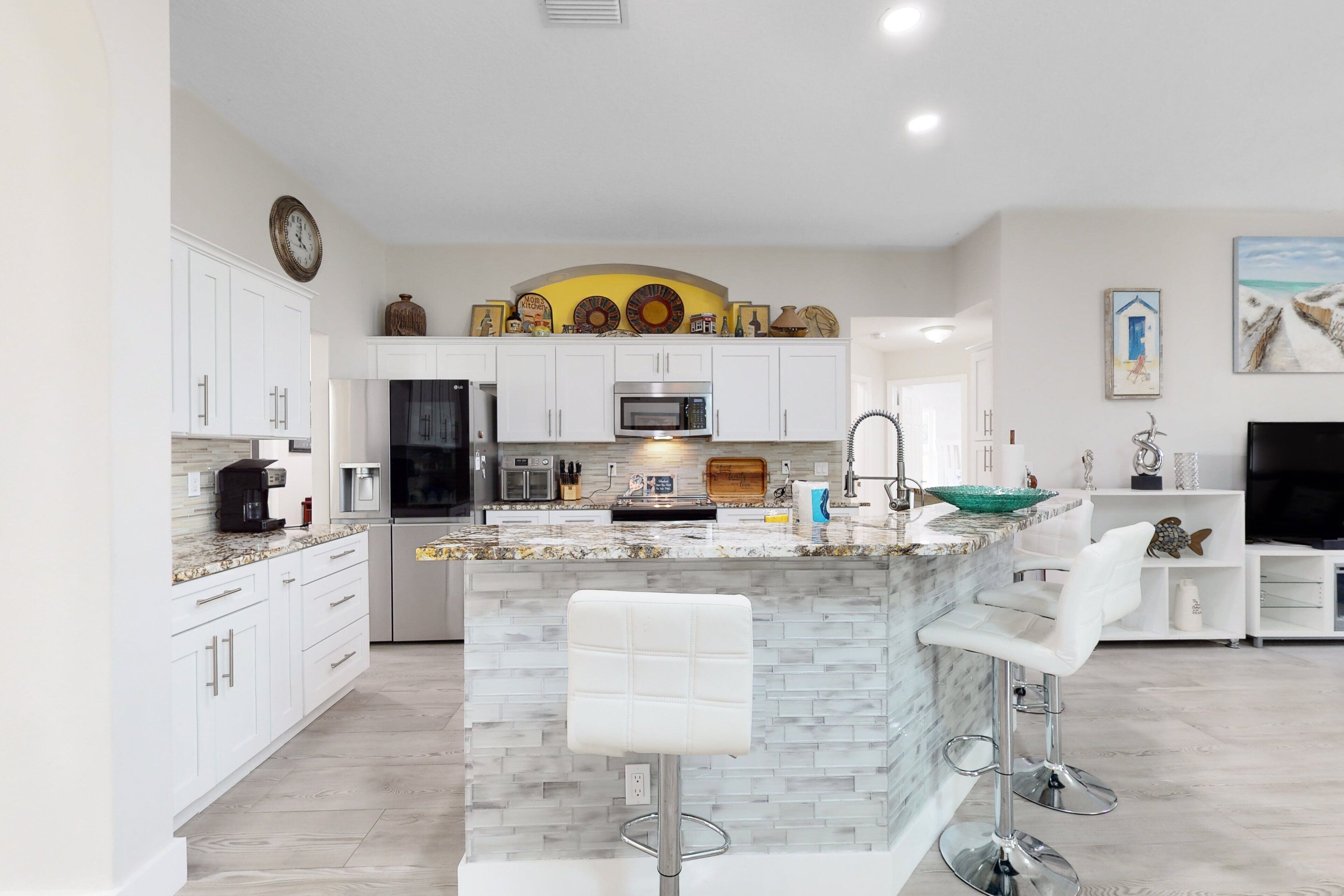 A modern kitchen with white cabinets, a central island with bar stools, a microwave, and a sink.