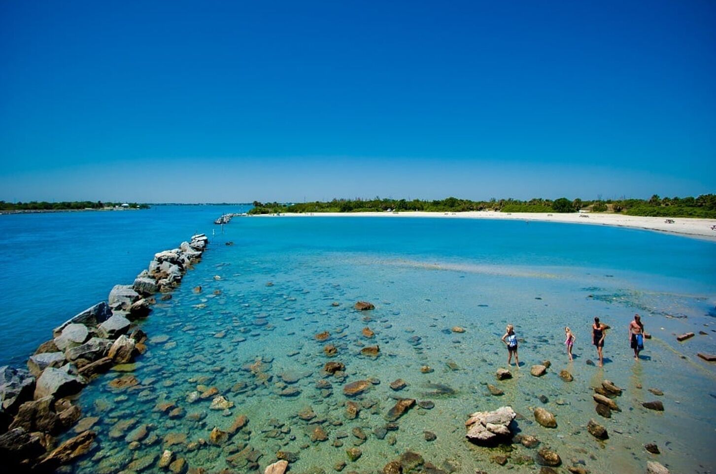 Uma praia calma com um molhe rochoso e faixa de areia.