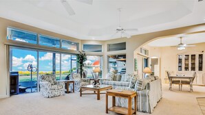 A spacious living room with large windows, a ceiling fan, and a dining area with a table and chairs. - 861 S Atlantic Ave (Cocoa Beach)